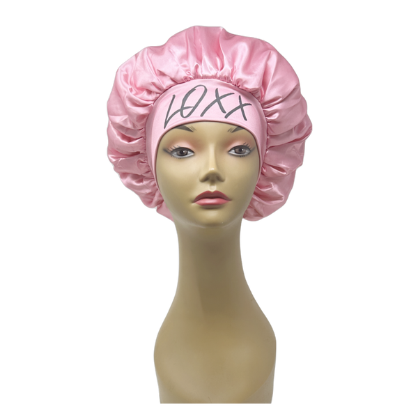Pink satin bonnet with elastic band, perfect for protecting hair while sleeping, featuring logo design.